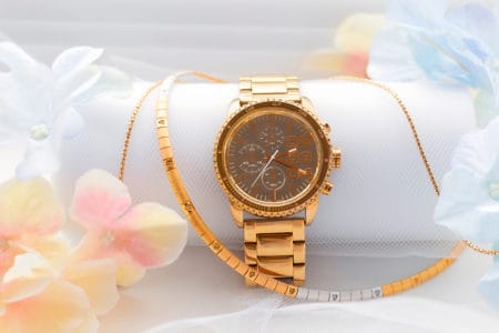 Gold female wristwatch combined with luxury jewerly above white airy background decorated bu flower petals