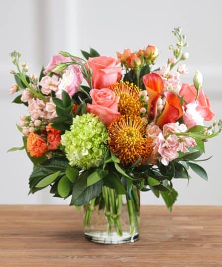 Peach roses, fragrant stock, delicate lisianthus, mini calla, exotic pincushion protea and southern hydrangea artfully designed in a chic decor vase to enjoy for years to come.