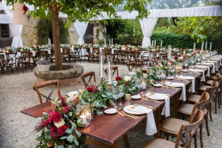 in backyard of villa in Tuscany there is a reception wooden table decorated with cotton and eucalyptus compositions, glasses, candles and plates are placed on table